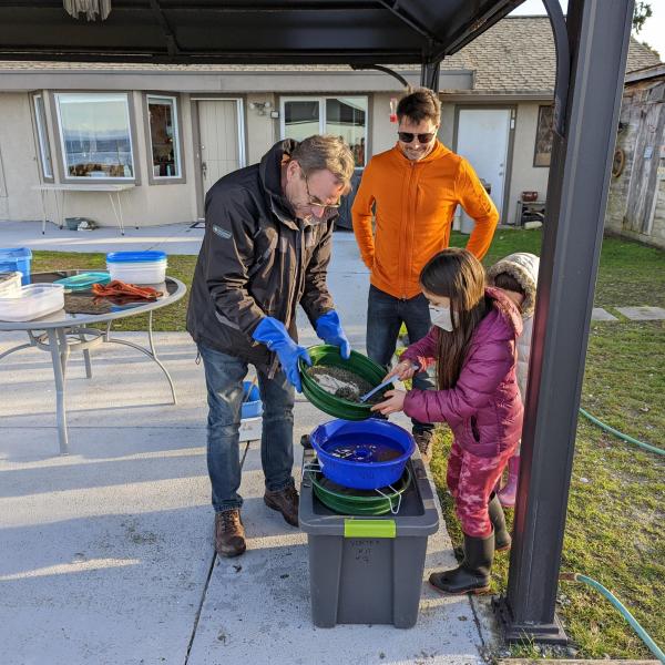 Two men and a young girl processing a sample through a vortex in a backyard